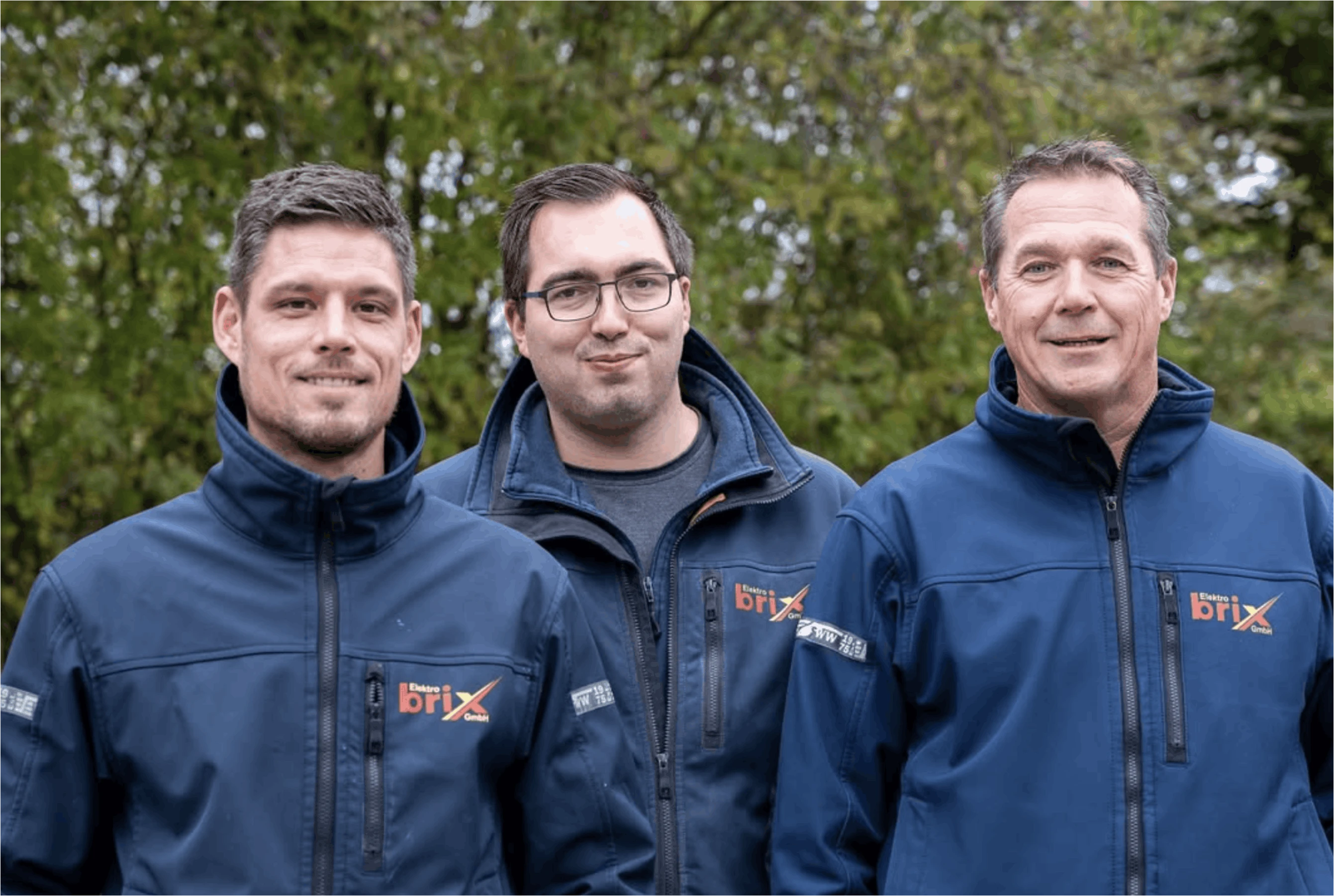 Drei Mitarbeiter von Elektro Brix in dunkelblauen Jacken mit Elektro Brix Logo